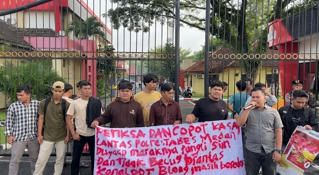 Sejumlah mahasiswa yang tergabung dalam AMPK SU menggelar aksi demonstrasi di depan pintu gerbang Mapolda Sumut. Massa membawa spanduk berisi desakan pemeriksaan dan pencopotan Kasat Lantas Polrestabes Medan terkait dugaan maraknya pungli SIM dan penanganan kenalpot blong yang dinilai tidak becus. (Foto: Istimewa)
